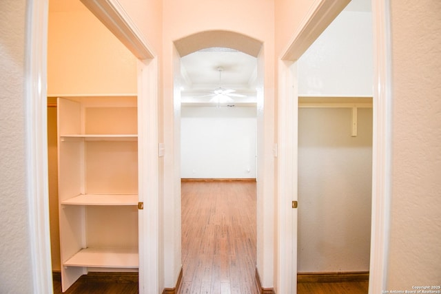 hallway with arched walkways, wood finished floors, and baseboards