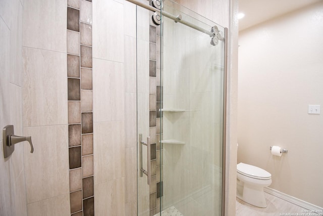 bathroom with a shower stall, toilet, and baseboards