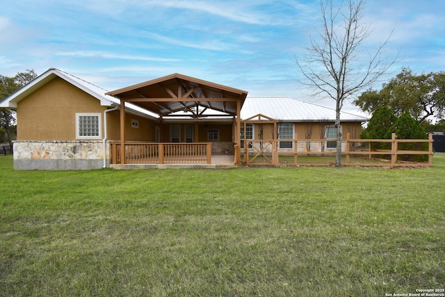 rear view of property with stone siding, stucco siding, fence, and a lawn