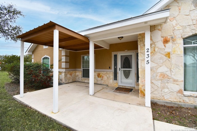 entrance to property with stone siding, a patio, and stucco siding