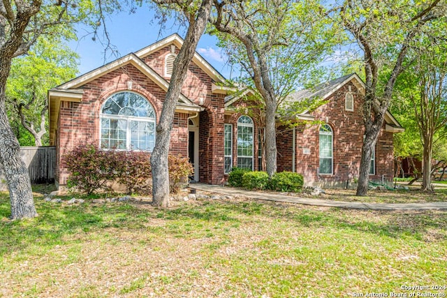 view of front facade featuring brick siding, fence, and a front lawn