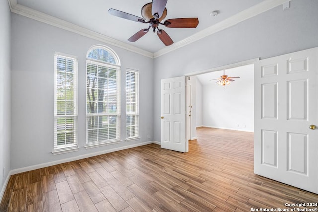 spare room featuring light wood-type flooring, ceiling fan, baseboards, and crown molding