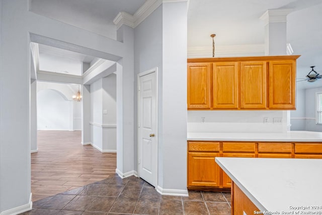 kitchen featuring arched walkways, light countertops, ornamental molding, brown cabinetry, and baseboards