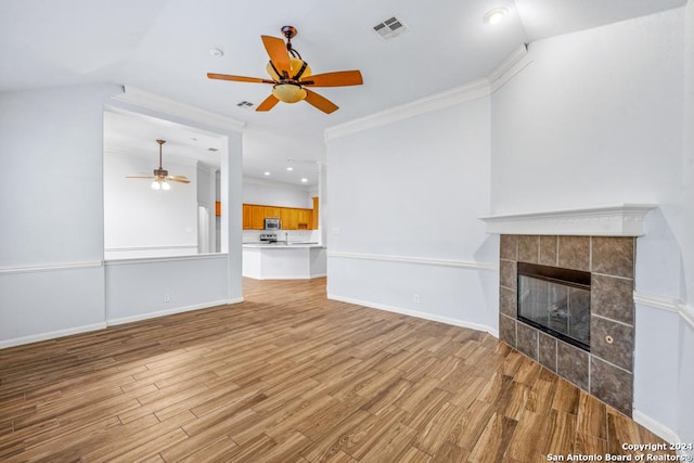 unfurnished living room featuring a tile fireplace, visible vents, baseboards, ornamental molding, and light wood-type flooring