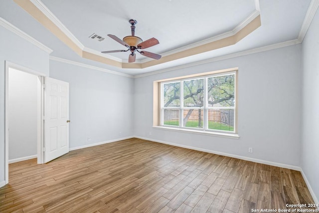 spare room with light wood-style floors, a raised ceiling, visible vents, and baseboards