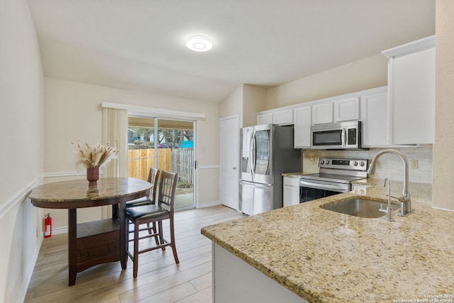 kitchen featuring light stone counters, a sink, white cabinetry, appliances with stainless steel finishes, and decorative backsplash