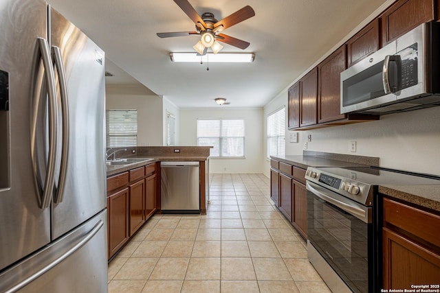 kitchen featuring dark countertops, ornamental molding, light tile patterned floors, stainless steel appliances, and a sink