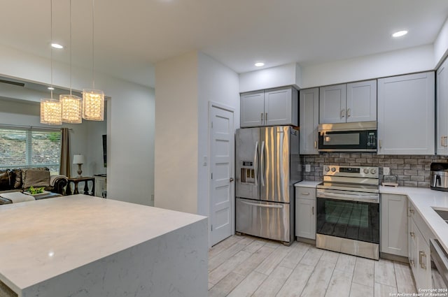 kitchen with appliances with stainless steel finishes, hanging light fixtures, gray cabinets, light countertops, and backsplash