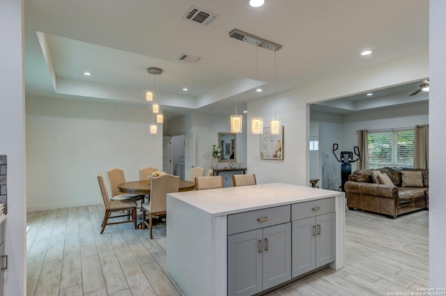 kitchen with light wood-style flooring, open floor plan, a tray ceiling, light countertops, and pendant lighting