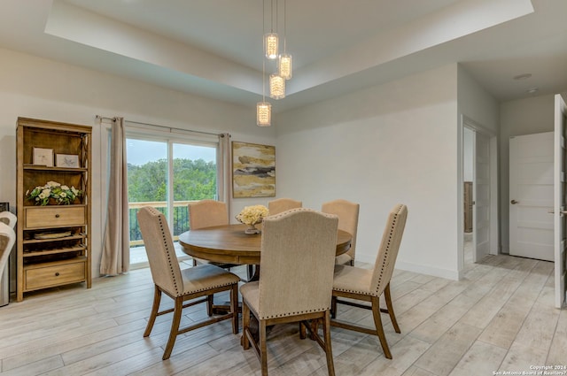 dining area with a tray ceiling, light wood-style flooring, and baseboards