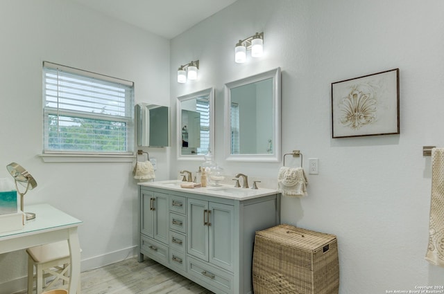 full bath with double vanity, wood finished floors, a sink, and baseboards