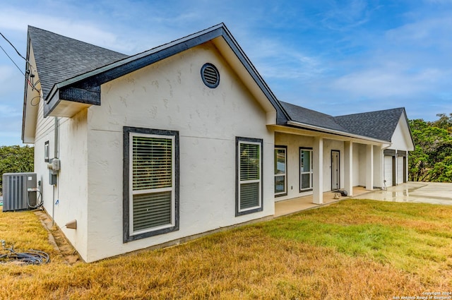 back of property with stucco siding, a shingled roof, a lawn, a garage, and cooling unit