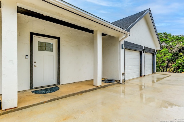 entrance to property featuring a garage, a shingled roof, and stucco siding