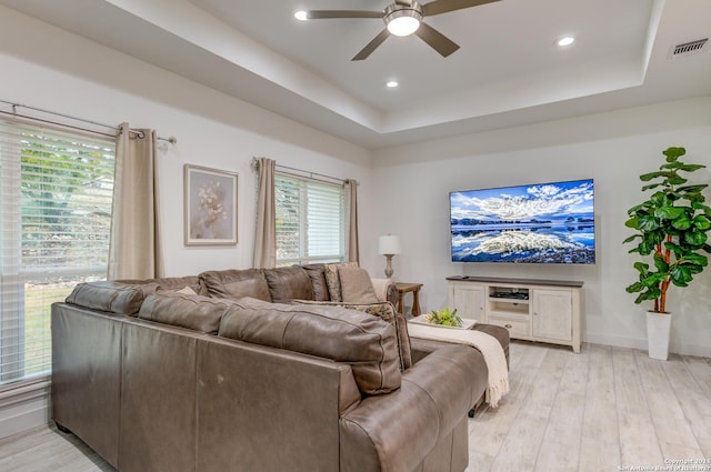 living room with baseboards, visible vents, ceiling fan, a tray ceiling, and light wood-type flooring