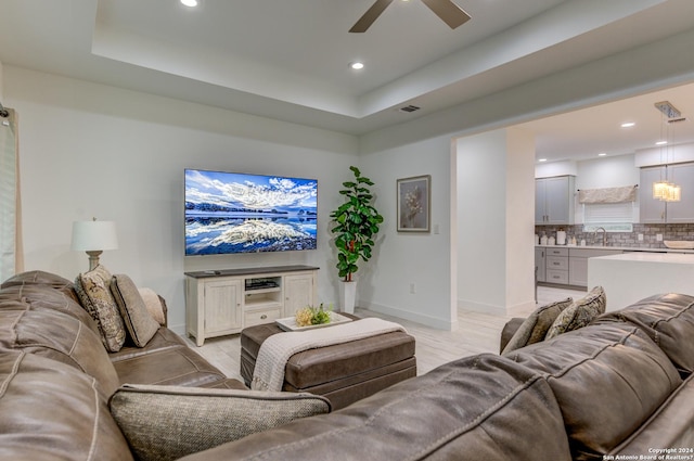 living area with light wood finished floors, baseboards, a raised ceiling, and a ceiling fan