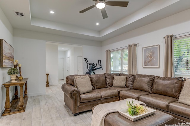 living area with light wood-style flooring, a raised ceiling, visible vents, and a healthy amount of sunlight