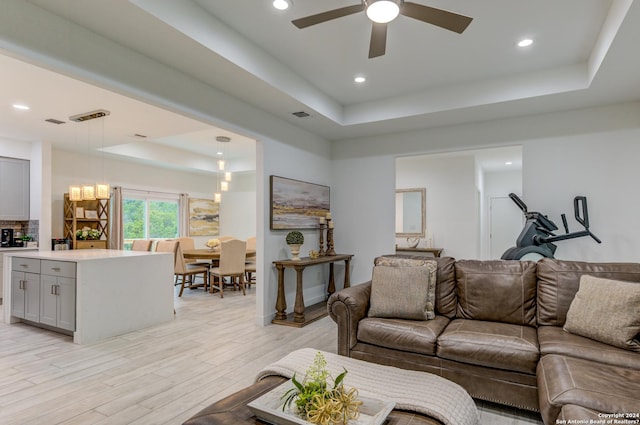 living room featuring light wood finished floors, a raised ceiling, a ceiling fan, and recessed lighting