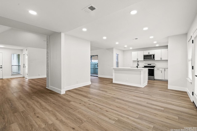 kitchen with a center island with sink, stainless steel appliances, light countertops, visible vents, and open floor plan