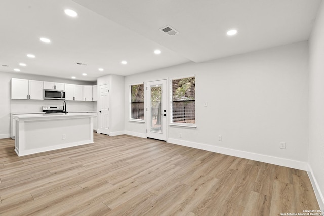 kitchen featuring visible vents, white cabinetry, light countertops, appliances with stainless steel finishes, and a center island with sink