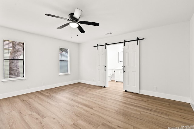 spare room with a barn door, visible vents, baseboards, a ceiling fan, and light wood-type flooring