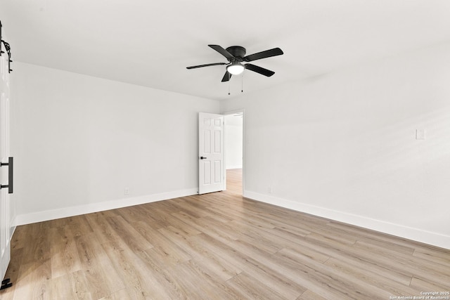 unfurnished room with light wood finished floors, a barn door, a ceiling fan, and baseboards