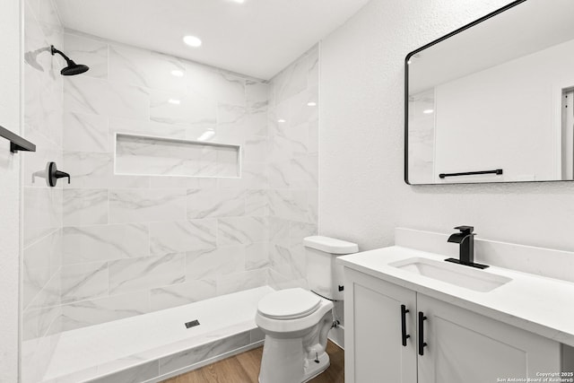 bathroom with a textured wall, toilet, wood finished floors, vanity, and a shower stall