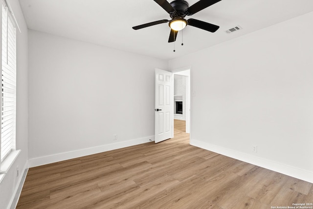 spare room featuring ceiling fan, a fireplace, visible vents, baseboards, and light wood-type flooring