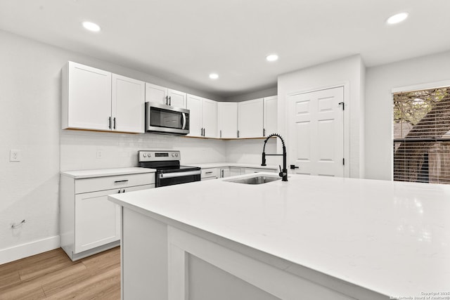 kitchen featuring light wood finished floors, recessed lighting, appliances with stainless steel finishes, white cabinets, and a sink