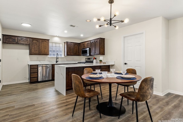 kitchen featuring dark brown cabinetry, dark wood finished floors, appliances with stainless steel finishes, light countertops, and pendant lighting