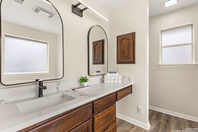 full bath featuring visible vents, vanity, baseboards, and wood finished floors