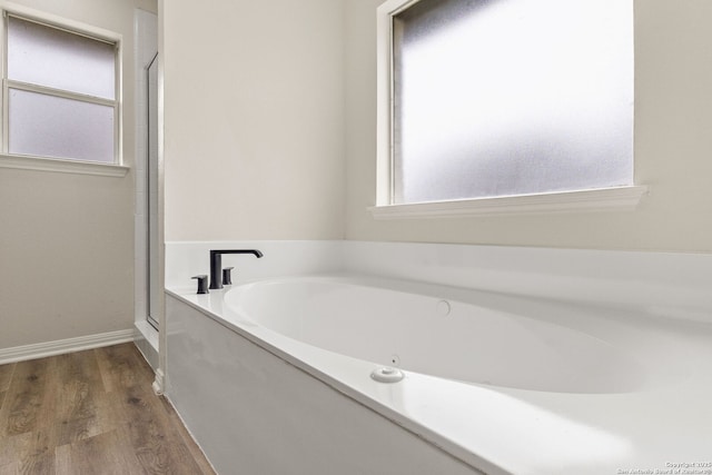 full bathroom featuring a bath, baseboards, and wood finished floors