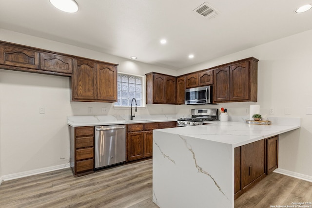 kitchen with visible vents, a peninsula, stainless steel appliances, light wood-type flooring, and a sink