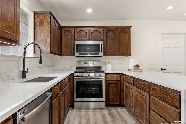 kitchen with dark brown cabinetry, recessed lighting, a sink, appliances with stainless steel finishes, and light wood finished floors