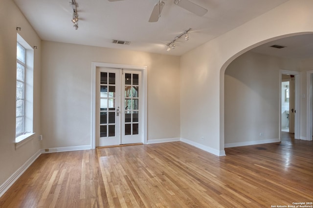 unfurnished room featuring light wood-type flooring, visible vents, arched walkways, and french doors