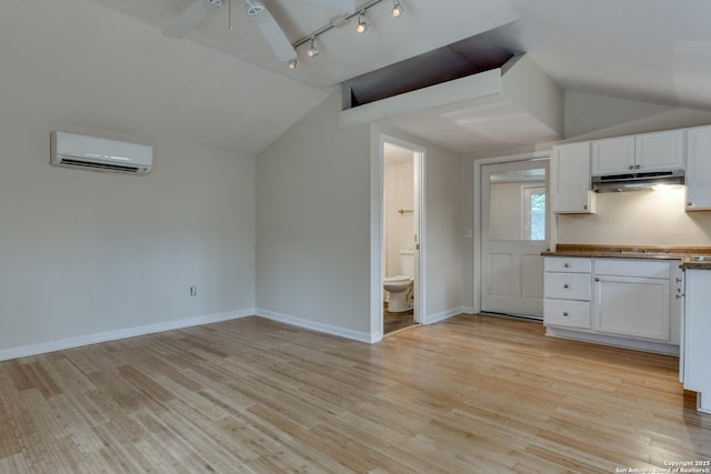 kitchen featuring lofted ceiling, under cabinet range hood, white cabinets, and a wall mounted air conditioner