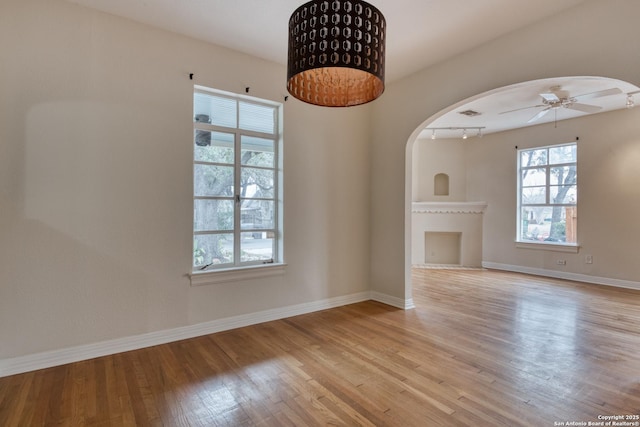 unfurnished living room with arched walkways, ceiling fan, light wood-type flooring, and baseboards