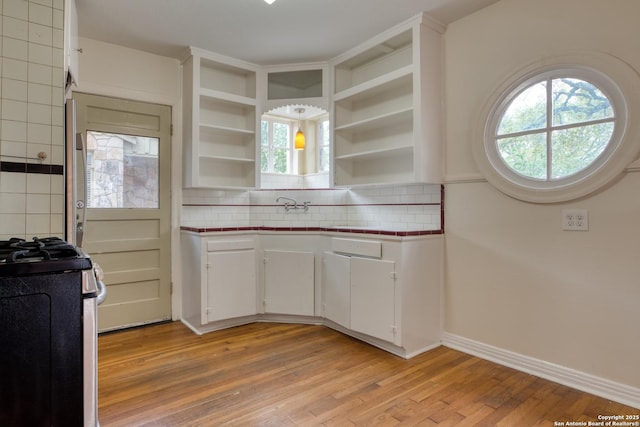 kitchen featuring open shelves, stainless steel stove, light wood-style flooring, decorative backsplash, and plenty of natural light