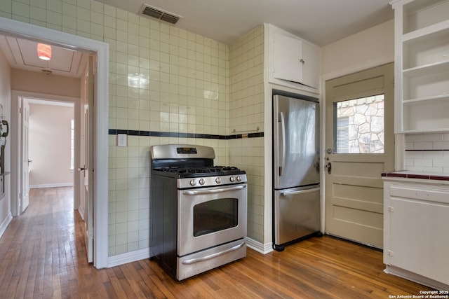 kitchen with stainless steel appliances, visible vents, tile walls, white cabinets, and light wood-type flooring