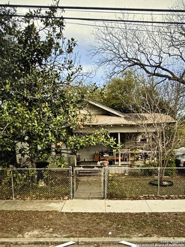 view of property hidden behind natural elements featuring covered porch, a fenced front yard, and a gate