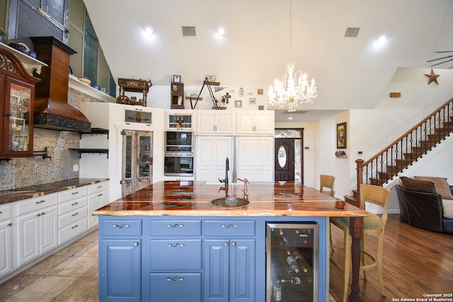 kitchen featuring wine cooler, wood counters, white cabinets, blue cabinetry, and glass insert cabinets