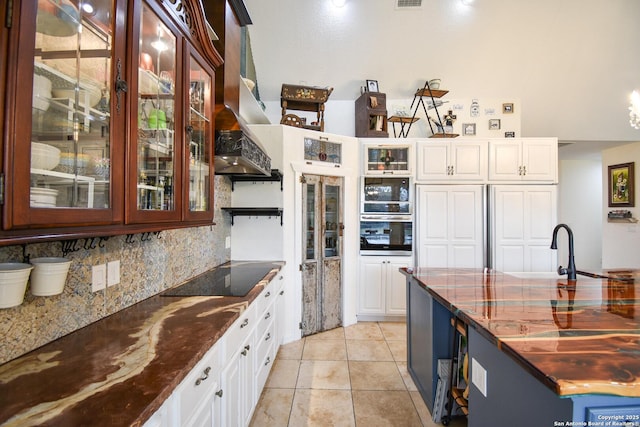 kitchen featuring glass insert cabinets, black electric stovetop, white cabinetry, and dark stone countertops