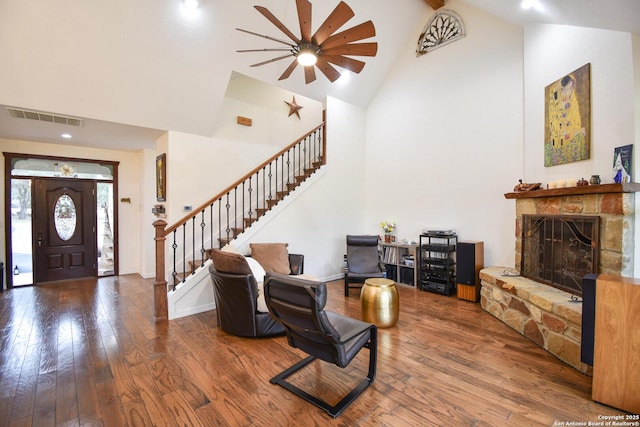 foyer featuring high vaulted ceiling, a stone fireplace, wood finished floors, visible vents, and stairs