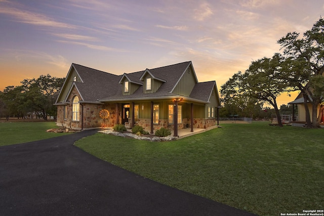 view of front of property with aphalt driveway, a porch, board and batten siding, a front yard, and stone siding