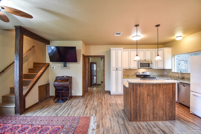 kitchen with a kitchen island, visible vents, appliances with stainless steel finishes, light stone countertops, and decorative light fixtures