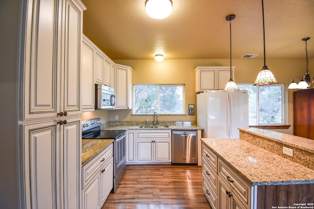 kitchen featuring light stone counters, decorative light fixtures, stainless steel appliances, white cabinetry, and a sink