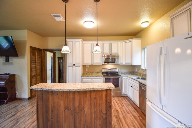 kitchen featuring visible vents, hanging light fixtures, appliances with stainless steel finishes, a sink, and light stone countertops