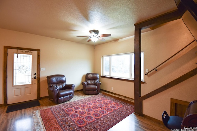 living area featuring baseboards, ceiling fan, wood finished floors, stairs, and a textured ceiling