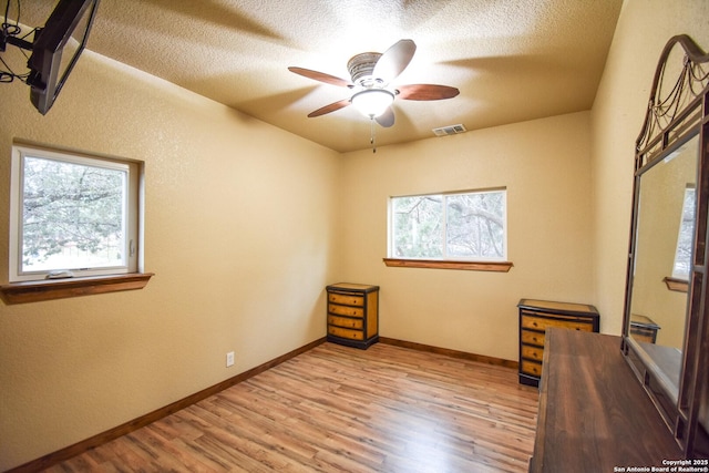 spare room featuring light wood-type flooring, visible vents, a textured ceiling, and baseboards