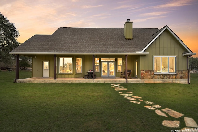 back of house featuring roof with shingles, a chimney, board and batten siding, and a yard