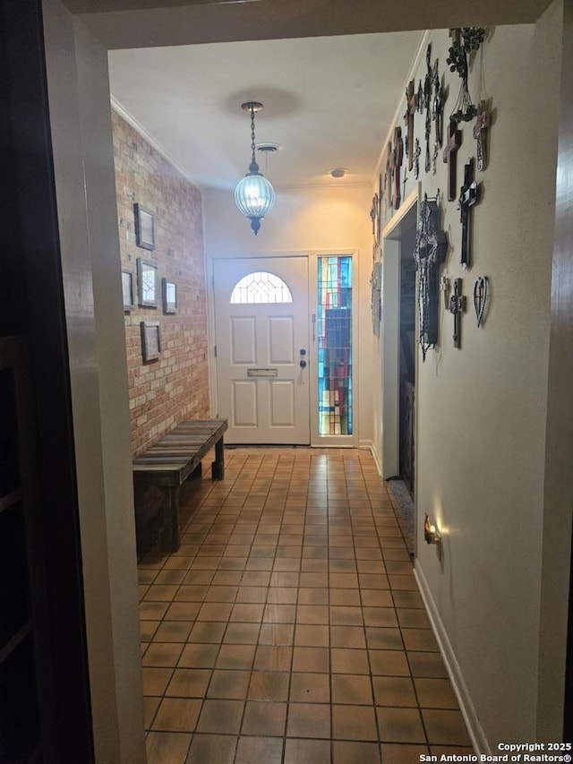 foyer featuring ornamental molding, tile patterned flooring, baseboards, and brick wall